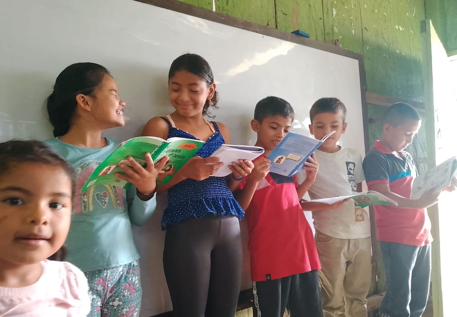 Children standing in front of a whiteboard, smiling and reading books